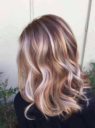 Schulterlanges, gewelltes Haar mit modernen blonden Balayage-Highlights im Freien.