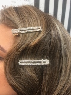 Zwei glitzernde Haarspangen mit Strasssteinen schmücken welliges braunes Haar.