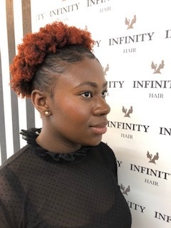 Frau mit natürlicher Afro-Frisur vor Infinity Hair Salon Werbewand, Haarstyling Beispiel.